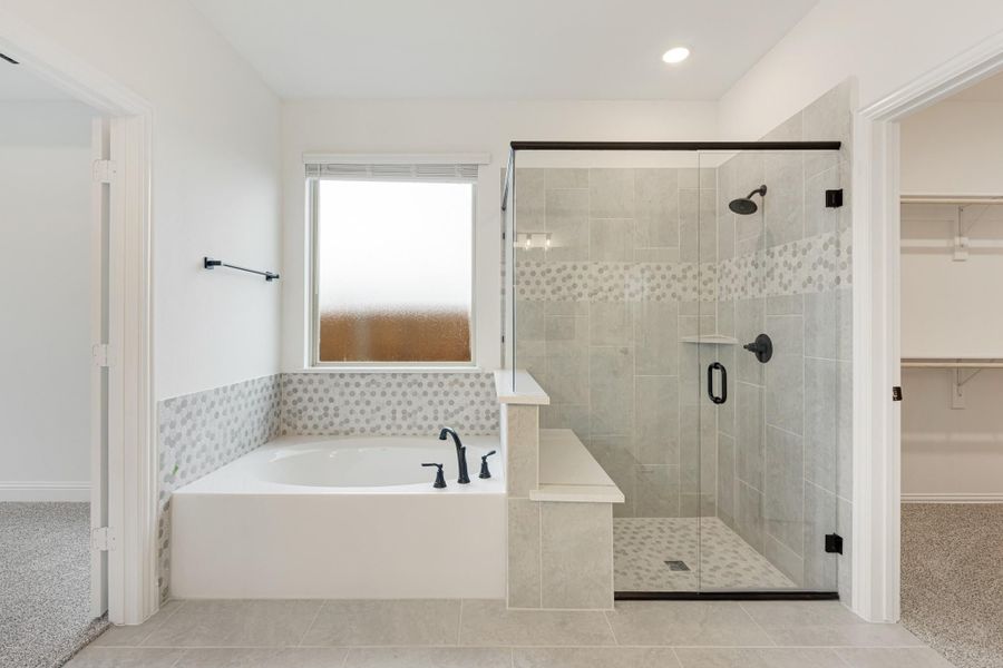 Master bathroom with soaking tub, glass-enclosed shower, tile surround, and walk-in closet entrance