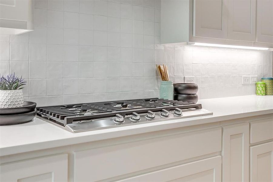 Kitchen with stainless steel gas stovetop, light countertops, white cabinetry, and tasteful backsplash Kitchen with stainless steel gas stovetop, light countertops, white cabinetry, and tasteful backsplash