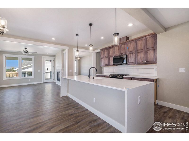 A kitchen from a completed Fort Latham, featuring darker stained cabinets and flooring plus a waterfall Quartz counter. Breakfast bars on kitchen islands are standard for Benchmark