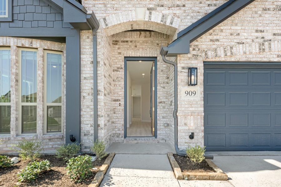 Brick home entrance with arched doorway, gray front door, and attached garage at address 909