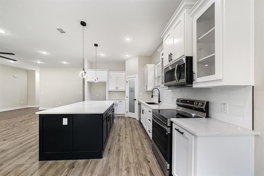 Kitchen featuring appliances with stainless steel finishes, light wood-style flooring, decorative backsplash, white cabinetry, and a center island Kitchen featuring appliances with stainless steel finishes, light wood-style flooring, decorative backsplash, white cabinetry, and a center island