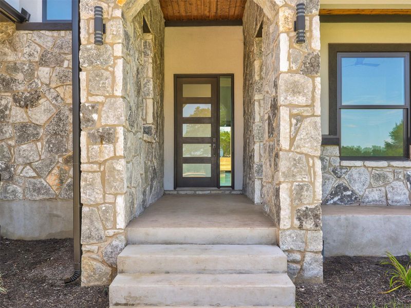 Natural stone masonry frames a recessed glass-paneled entry door complete with concrete steps.