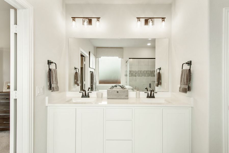 Bathroom with double sink vanity, white cabinets, large mirror, and glass shower in background