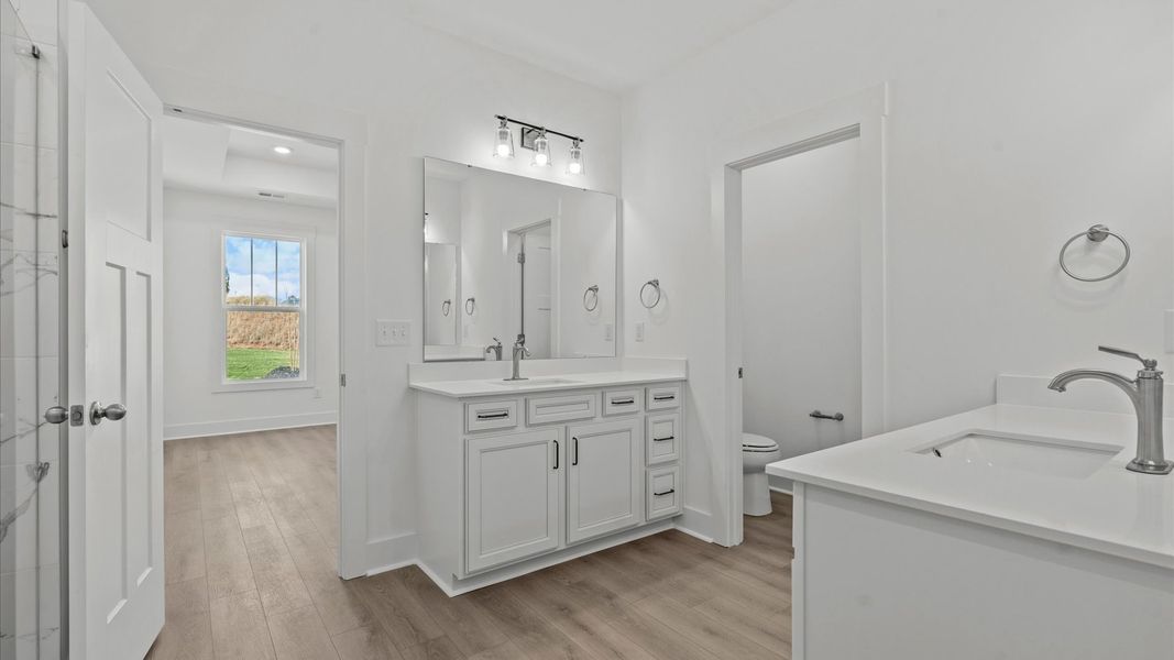 Superior en-suite primary bathroom with stylish separate vanities and tiled walk-in Roman shower