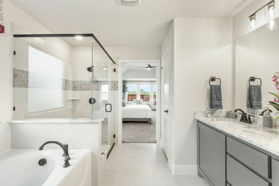 Master bathroom with soaking tub, glass shower, and double vanity with marble countertops and gray cabinets