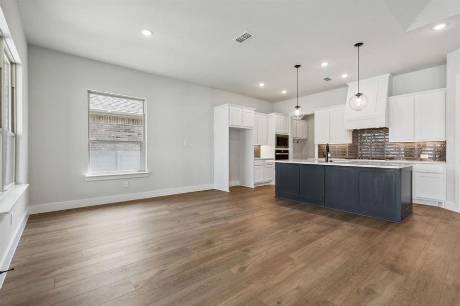 Kitchen with wood-type flooring, hanging light fixtures, white cabinets, and a kitchen island with sink