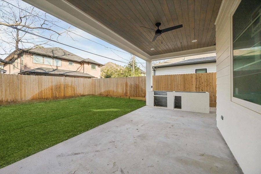 BACKYARD - Covered patio extends living space outdoors with a wood-clad ceiling, ceiling fan, and built in grill station ready for easy entertaining. Open sightlines to the yard allow for seamless indoor outdoor flow while maintaining privacy behind full fencing. -- Construction as of 1/5/26