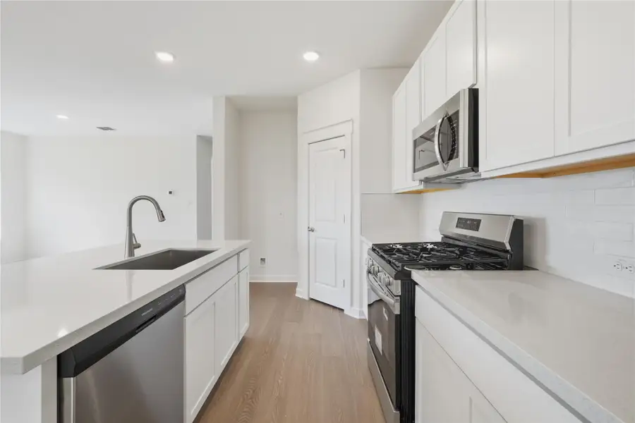 Kitchen featuring appliances with stainless steel finishes, light wood finished floors, white cabinetry, recessed lighting, and light stone countertops Kitchen featuring appliances with stainless steel finishes, light wood finished floors, white cabinetry, recessed lighting, and light stone countertops