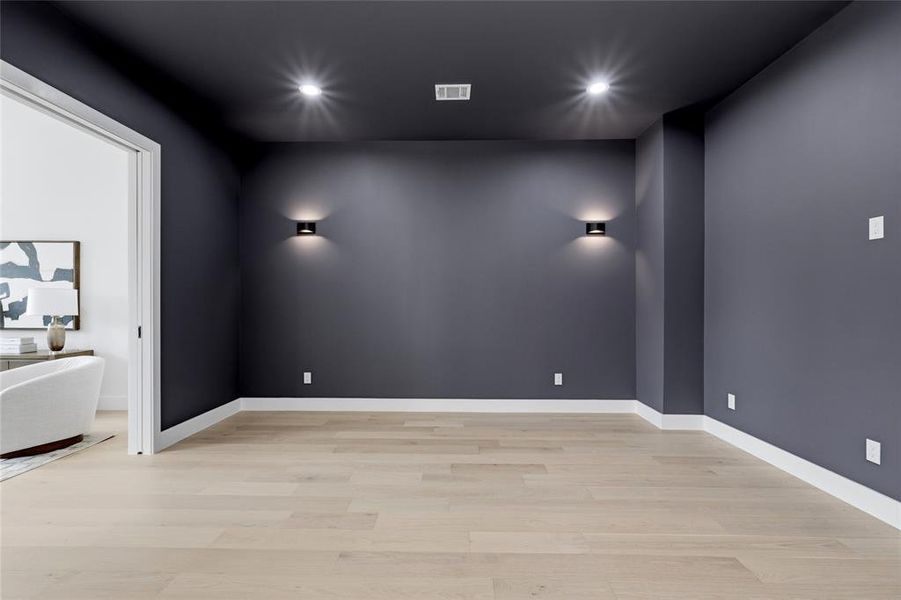 Spacious room with dark gray walls, recessed ceiling lighting, and light wood-finish flooring Spacious room with dark gray walls, recessed ceiling lighting, and light wood-finish flooring