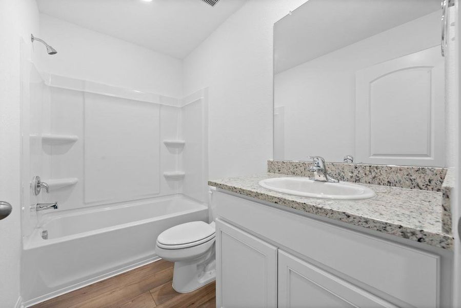 Secondary bathroom includes granite counters, designer white cabinetry and luxury vinyl plank flooring.