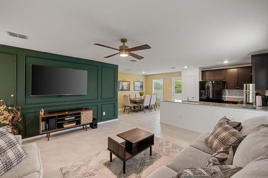 Living room featuring light tile patterned floors, a decorative wall, and ceiling fan