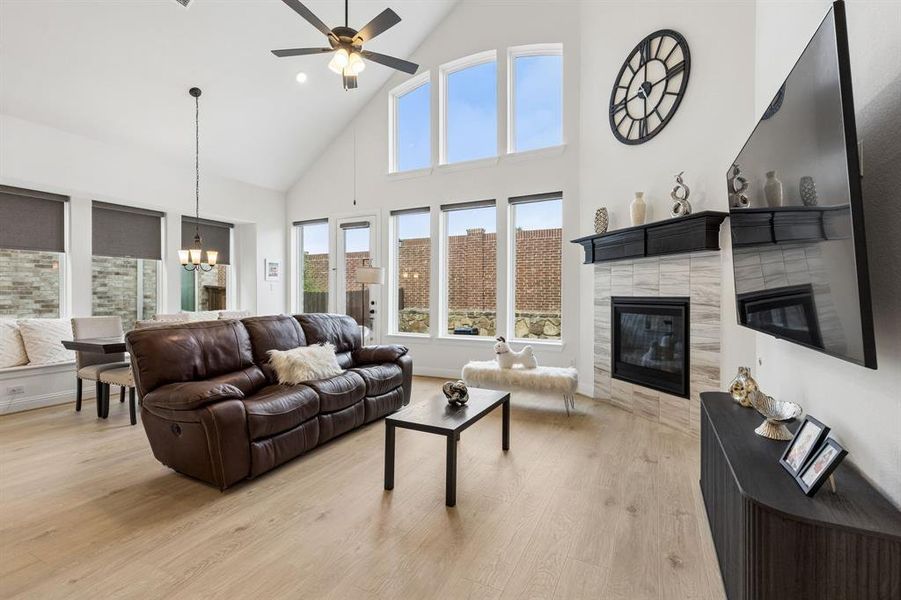 Spacious living area featuring a vaulted ceiling with a ceiling fan, a fireplace with a light-toned tile surround and dark mantel, and wood-finish flooring