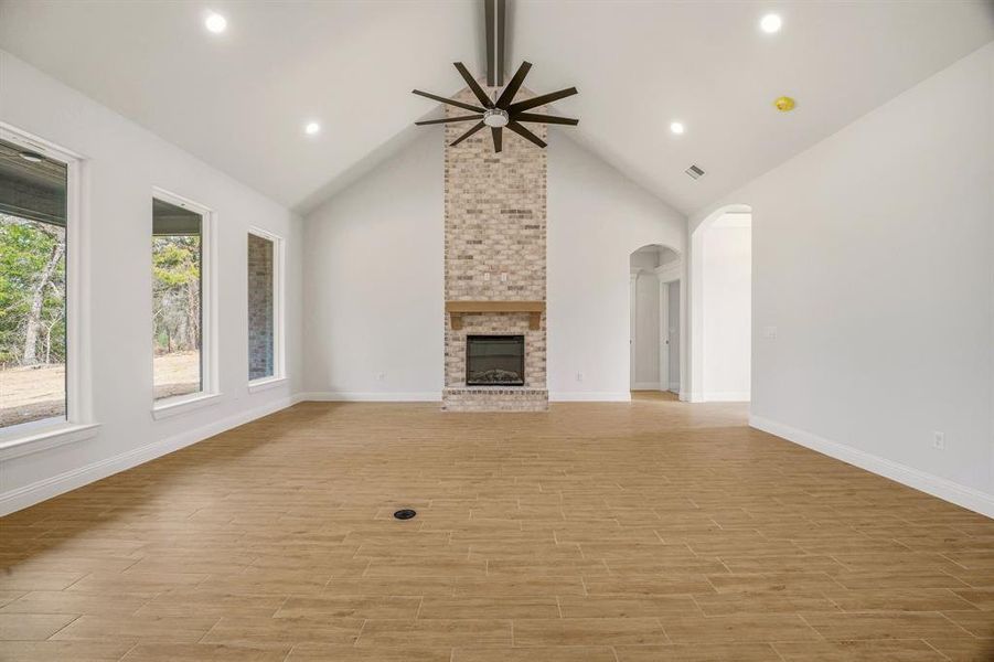 Unfurnished living room featuring a brick fireplace, wood finish floors, a ceiling fan, recessed lighting, and arched walkways Unfurnished living room featuring a brick fireplace, wood finish floors, a ceiling fan, recessed lighting, and arched walkways