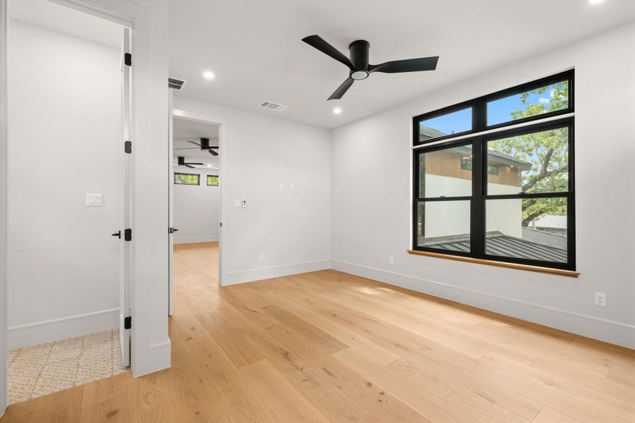 Warm wood flooring and a large black-framed window highlight this serene modern bedroom.