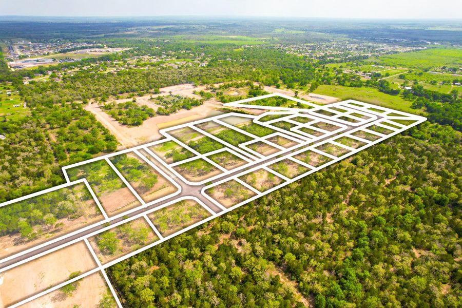 Aerial view of a sprawling land development with clearly marked plots and new roads, surrounded by abundant natural greenery.