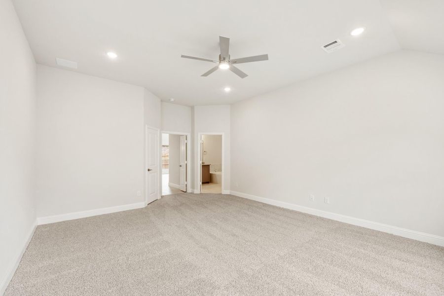Empty bedroom with carpet flooring, ceiling fan, and open door leading to ensuite bathroom