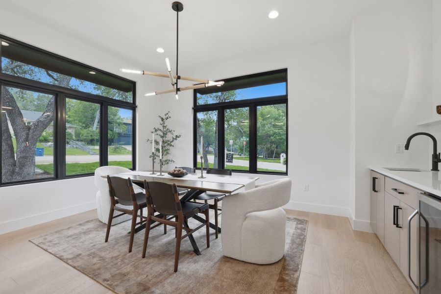 Dining area featuring expansive black-framed windows, a contemporary linear chandelier, light wood-finish flooring, and recessed lighting