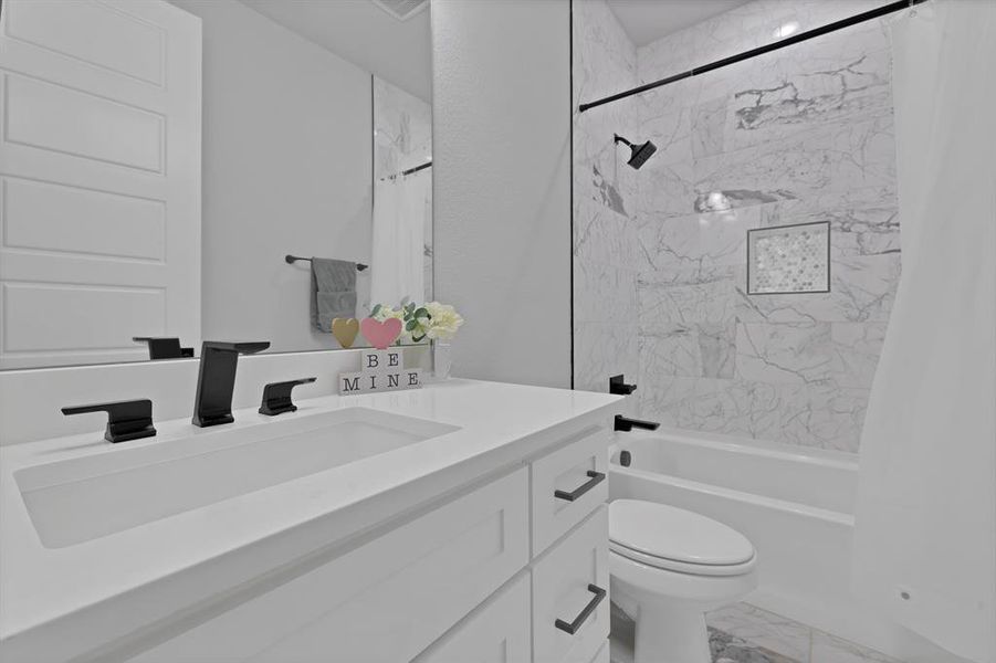 Bathroom with marble finish floor, vanity, shower / bath combo with shower curtain, and toilet