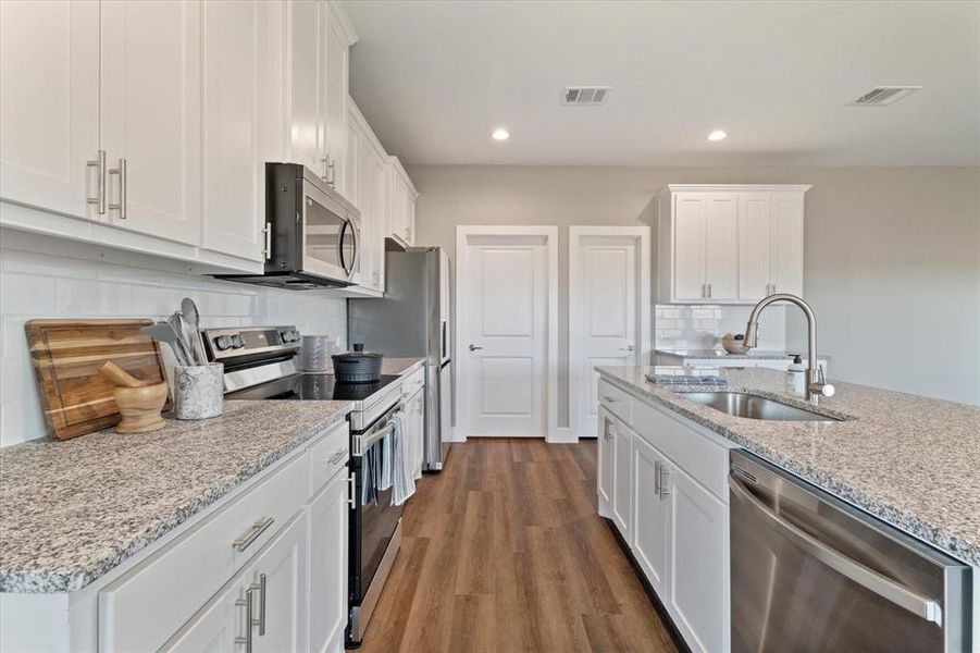 Kitchen featuring hardwood / wood-style floors, white cabinets, sink, tasteful backsplash, and stainless steel appliances Kitchen featuring hardwood / wood-style floors, white cabinets, sink, tasteful backsplash, and stainless steel appliances