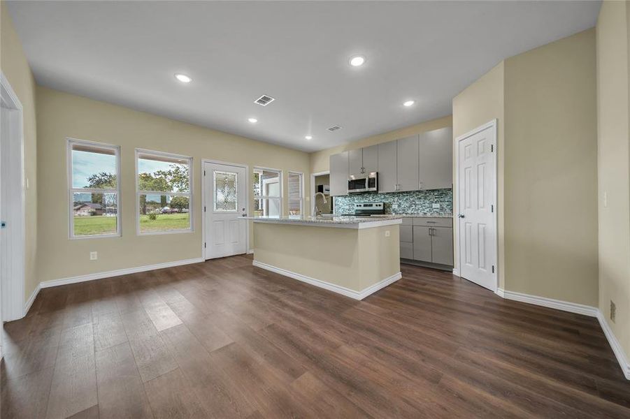 Kitchen with stainless steel appliances, decorative backsplash, dark wood-type flooring, a center island with sink, and gray cabinetry