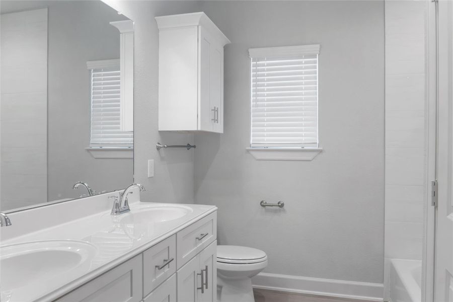This bathroom features a clean, modern design with dual sinks, a large mirror, white cabinetry, and a sleek, neutral color palette.