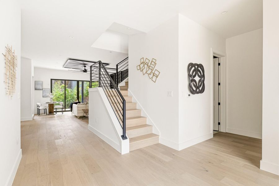 Bright interior featuring light wood-finish flooring, a modern staircase with black metal railings, and a recessed ceiling fan