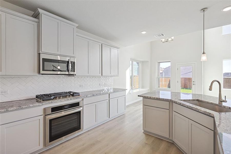 Kitchen featuring sink, light stone countertops, light wood-type flooring, appliances with stainless steel finishes, and tasteful backsplash