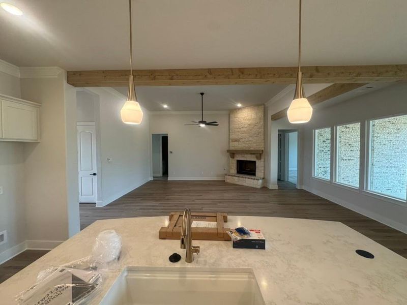 Open-concept living space with exposed wood-finish ceiling beams, wood-finish flooring, and a stone-clad fireplace Open-concept living space with exposed wood-finish ceiling beams, wood-finish flooring, and a stone-clad fireplace