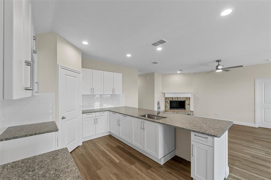 Spacious open-concept living area featuring a kitchen with white cabinetry, granite countertops, and a subway tile backsplash