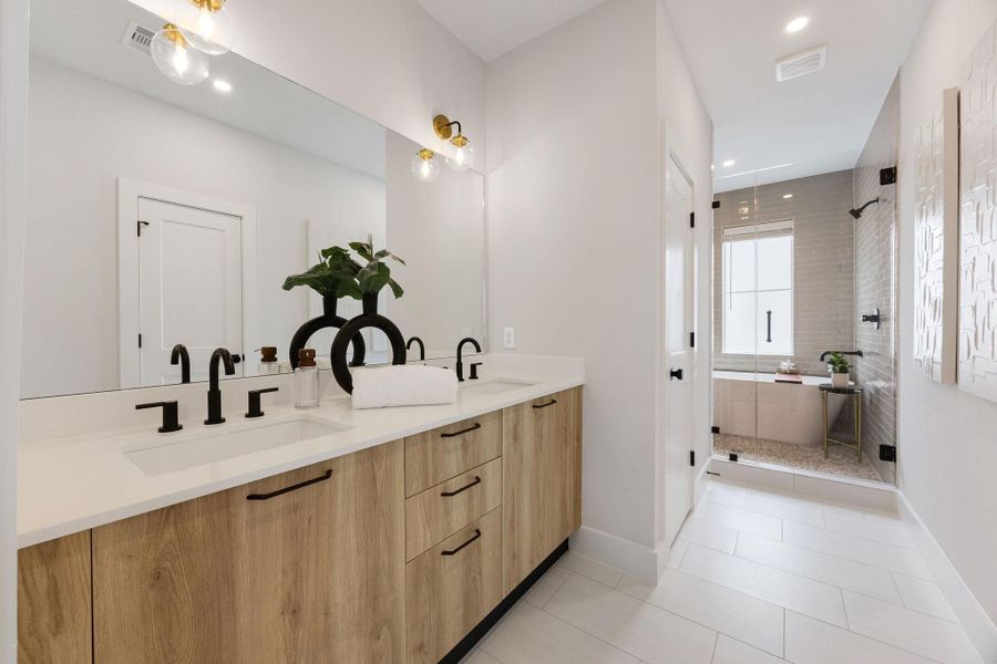 Spa-like primary bathroom featuring dual vanities, quartz countertops, designer fixtures, oversized mirrors, and a seamless modern design with upscale finishes throughout.