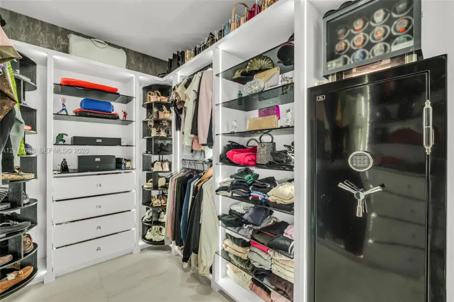 Custom closet system featuring white built-in cabinetry, vertical integrated LED lighting, open glass shelving, a rotating shoe rack, and an integrated heavy-duty floor safe Custom closet system featuring white built-in cabinetry, vertical integrated LED lighting, open glass shelving, a rotating shoe rack, and an integrated heavy-duty floor safe