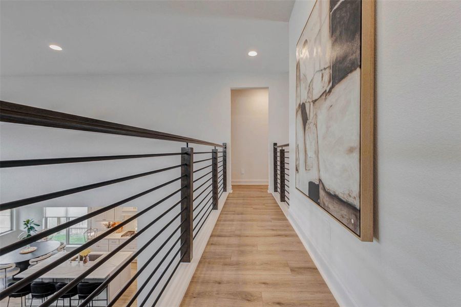This photo showcases a modern hallway with wood flooring and sleek metal railings, overlooking an open living area. The space is bright and airy, enhanced by contemporary wall art. This photo showcases a modern hallway with wood flooring and sleek metal railings, overlooking an open living area. The space is bright and airy, enhanced by contemporary wall art.