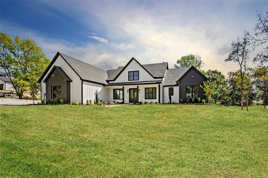 Modern farmhouse style home featuring a front lawn, a standing seam roof, roof with shingles, board and batten siding, and a metal roof Modern farmhouse style home featuring a front lawn, a standing seam roof, roof with shingles, board and batten siding, and a metal roof