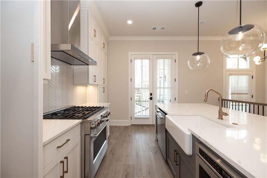 Kitchen featuring white cabinetry, appliances with stainless steel finishes, wall chimney range hood, pendant lighting, and sink