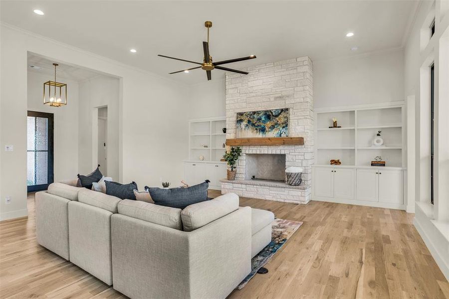 Living room with ornamental molding, a stone fireplace, light wood-type flooring, recessed lighting, and a ceiling fan Living room with ornamental molding, a stone fireplace, light wood-type flooring, recessed lighting, and a ceiling fan