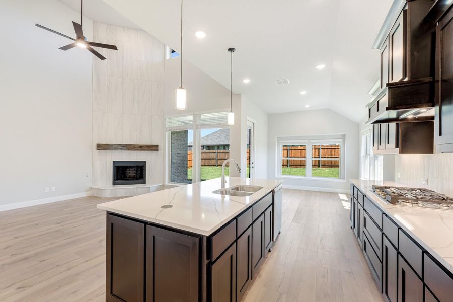 Open kitchen with dark cabinets, quartz island, and vaulted ceiling open to living room with fireplace Open kitchen with dark cabinets, quartz island, and vaulted ceiling open to living room with fireplace