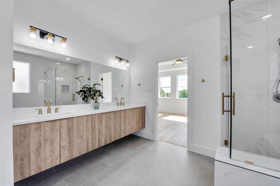The luxurious primary bath features quartz counters, brushed brass fixtures, dual sinks, lots of cabinets, a separate glass enclosed shower and a soaking tub.