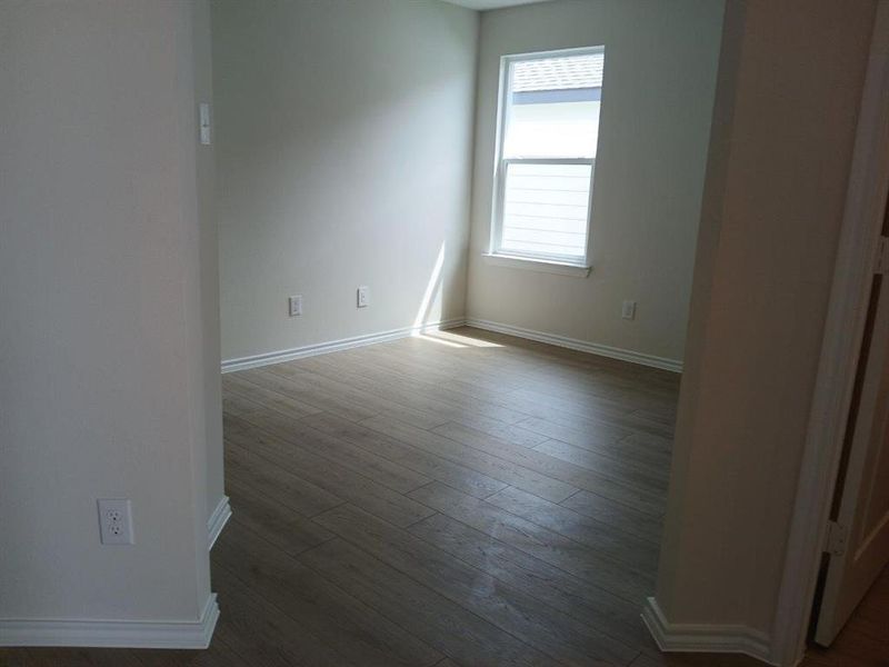 Room featuring wood-finish flooring, white baseboards, and neutral wall paint Room featuring wood-finish flooring, white baseboards, and neutral wall paint