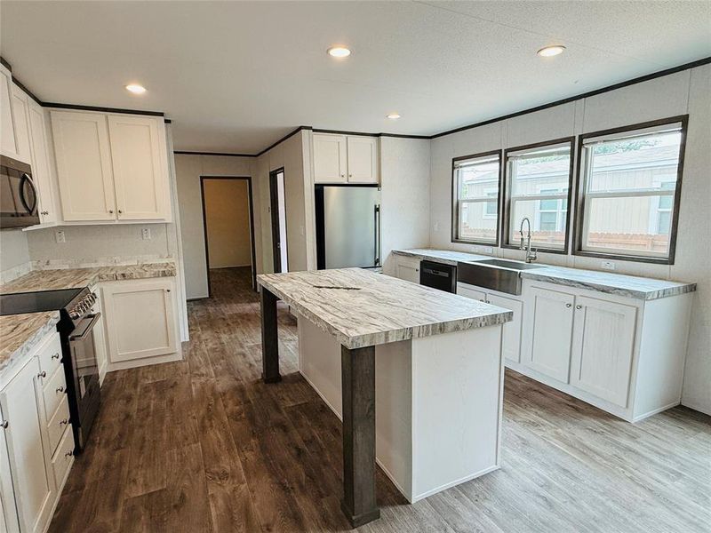 Kitchen featuring black appliances, wood finished floors, light countertops, and a sink
