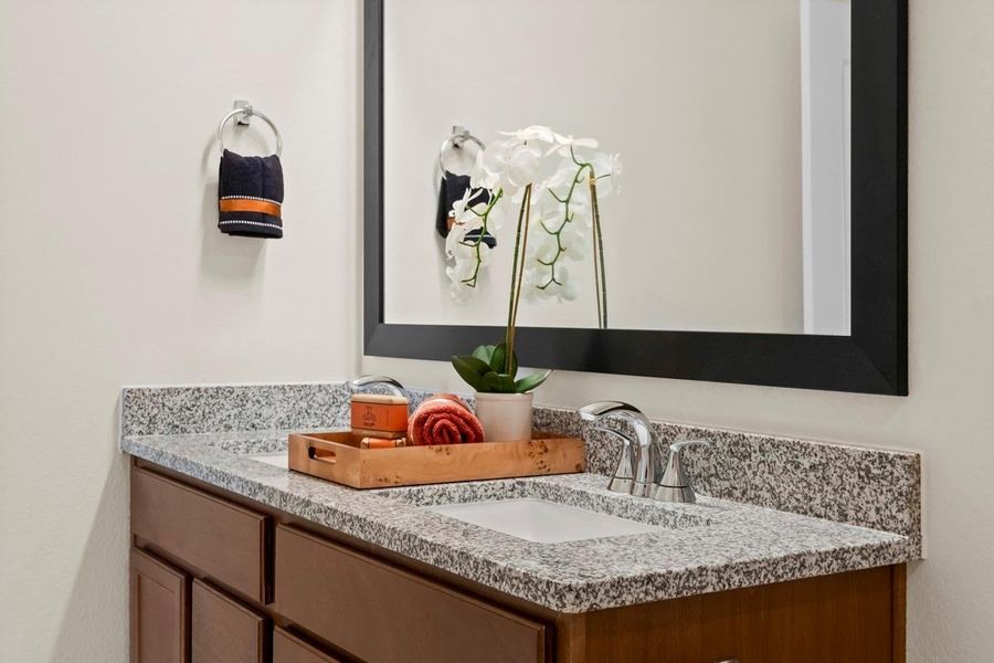 Secondary bath features tile flooring, bath/shower combo with tile surround, stained wood cabinets, beautiful granite countertops, framed mirror, sleek fixtures and modern finishes.