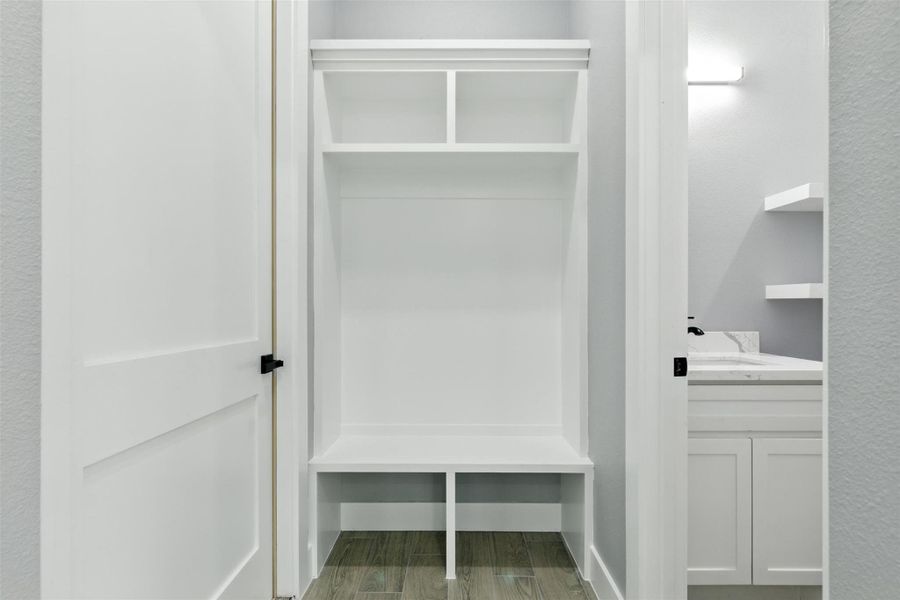 This photo showcases a small, functional mudroom area with a built-in white bench and storage cubbies. Adjacent is a bathroom with modern fixtures and a light gray color scheme. The space is efficient, ideal for organizing and quick access.
