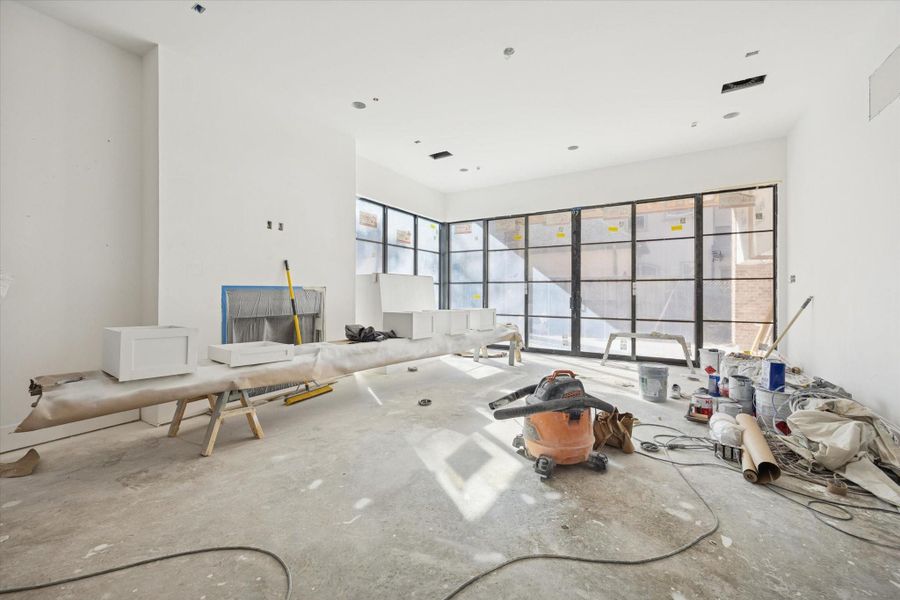 Bright, open-concept living room with sliding doors and expansive corner windows that seamlessly connect to the outdoor living space. Pictured February 2026.