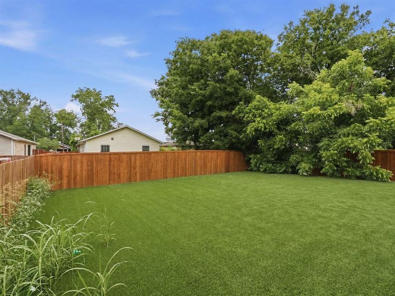 Expansive backyard featuring a uniform green lawn, a wood plank privacy fence, and mature trees providing natural screening Expansive backyard featuring a uniform green lawn, a wood plank privacy fence, and mature trees providing natural screening