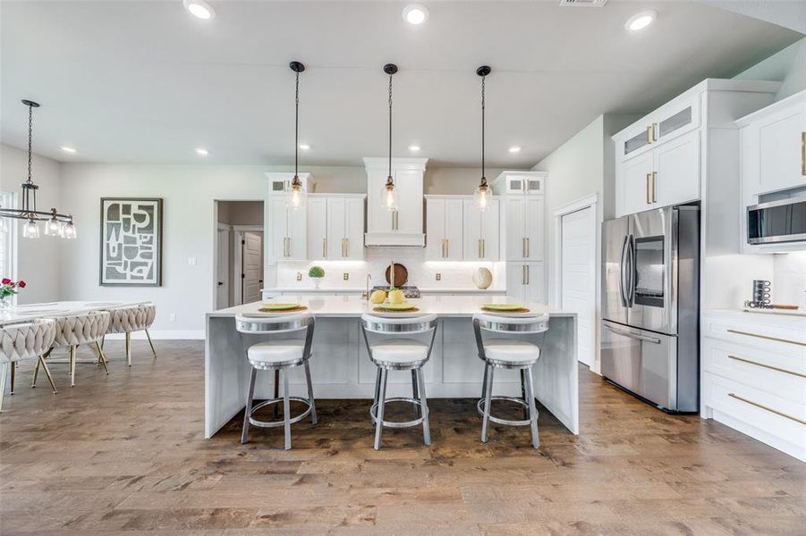 Kitchen featuring backsplash, pendant lighting, appliances with stainless steel finishes, light wood-type flooring, and a spacious island