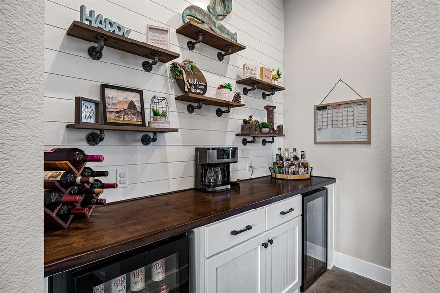 Indoor dry bar with wooden counters, white cabinetry, wine cooler, and a textured wall Indoor dry bar with wooden counters, white cabinetry, wine cooler, and a textured wall