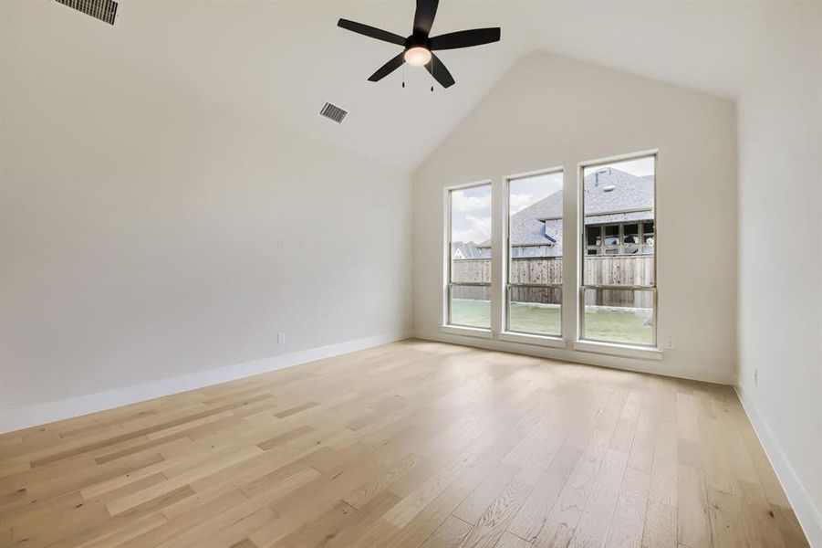 Vaulted ceiling room featuring light wood-finish flooring, three tall windows, a ceiling fan, and white baseboards Vaulted ceiling room featuring light wood-finish flooring, three tall windows, a ceiling fan, and white baseboards