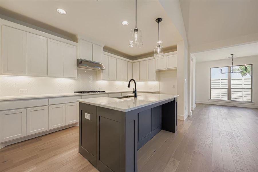 Kitchen featuring white cabinetry, decorative backsplash, decorative light fixtures, light stone counters, and light wood-style flooring Kitchen featuring white cabinetry, decorative backsplash, decorative light fixtures, light stone counters, and light wood-style flooring