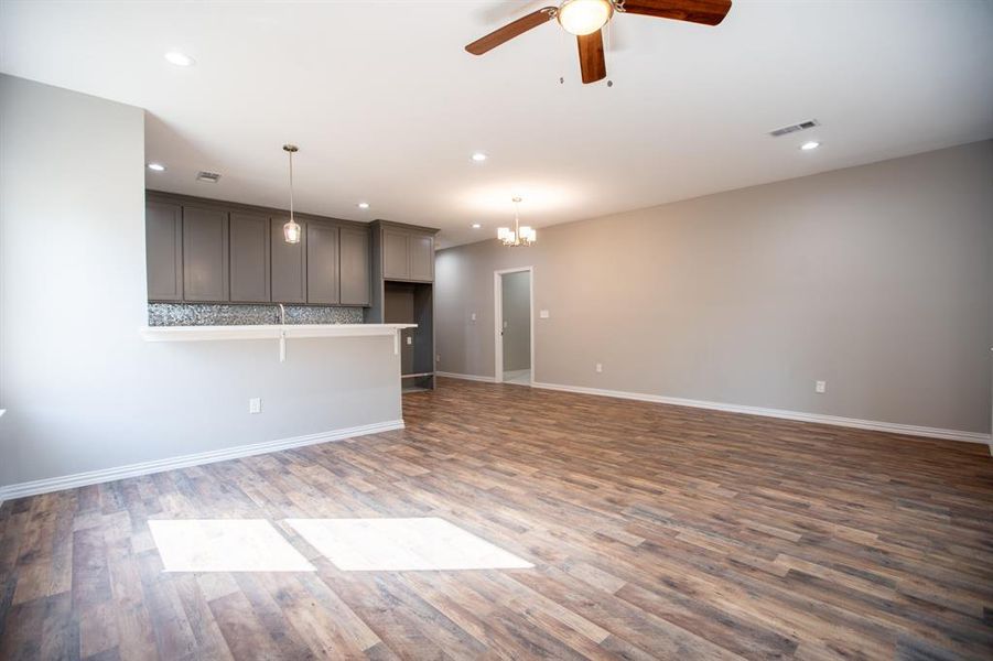 Unfurnished living room with ceiling fan with notable chandelier and hardwood / wood-style flooring