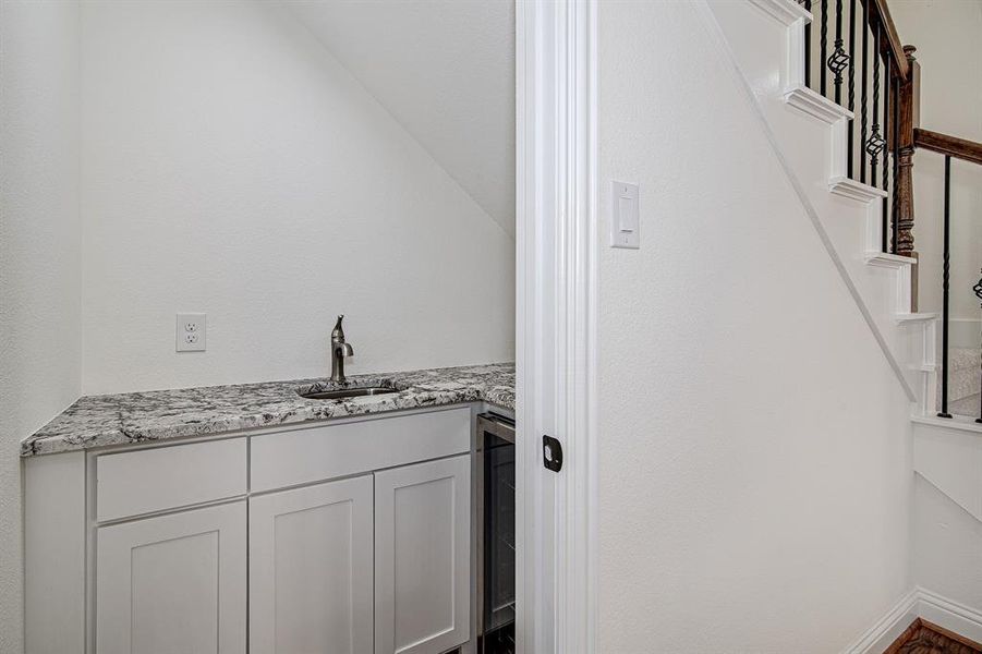 Bar featuring light stone countertops, white cabinetry, sink, and wine cooler