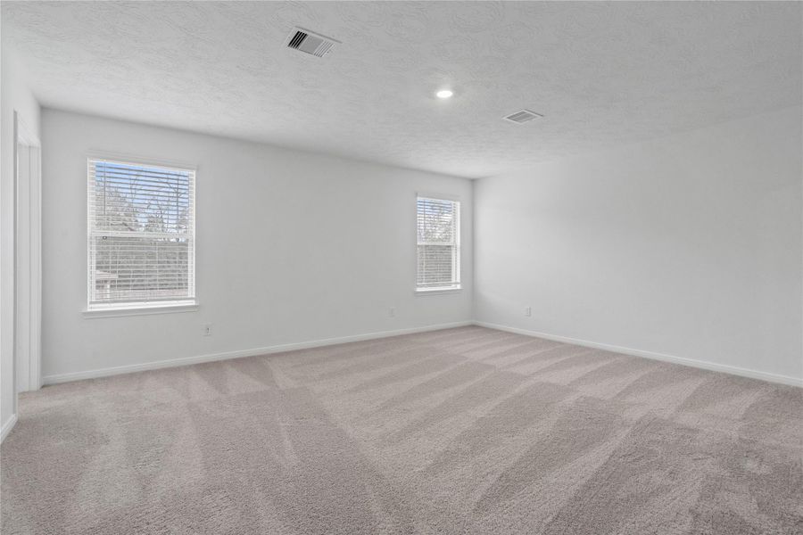 Natural light fills this elegant primary bedroom, creating a bright and inviting space to start and end your day. It features plush carpeting, high ceilings, recessed lighting, neutral tone paint, ensuite bathroom, and walk-in closet.